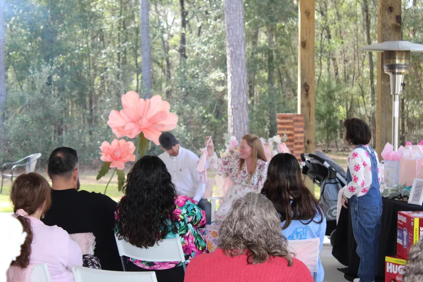 Guests seated at a baby shower under the pavilion, pink decorations behind them