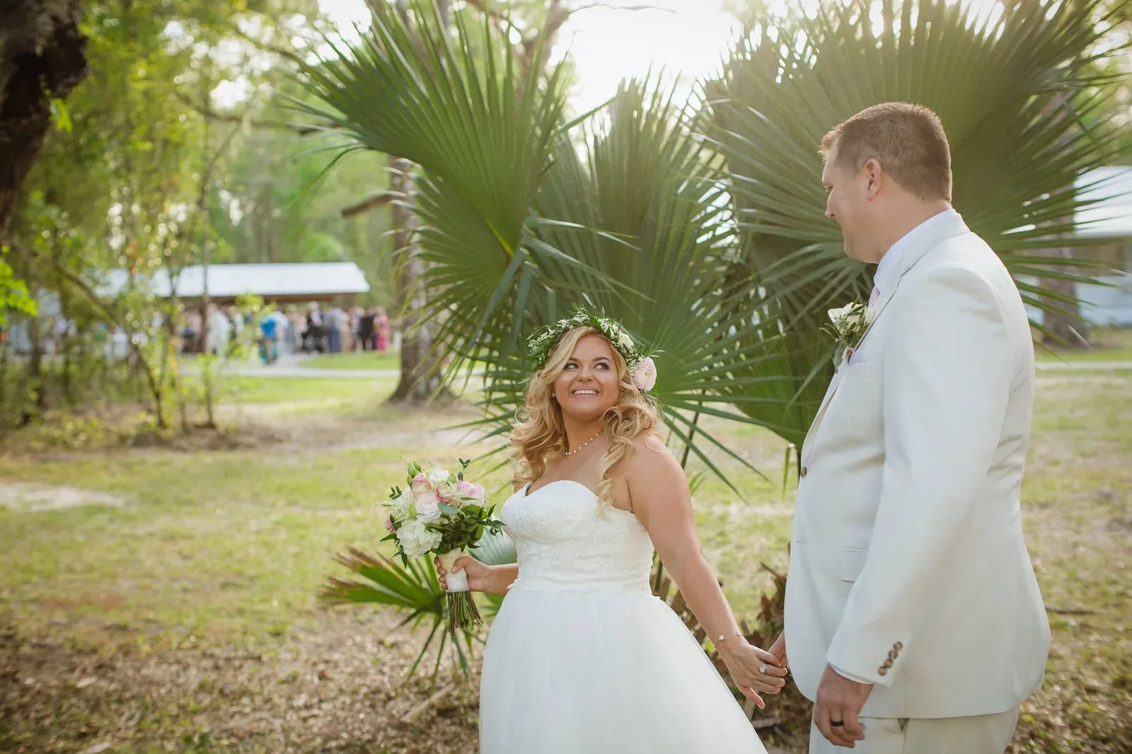 A groom leaning in to kiss his bride beneath a large oak, her train spread across the grass