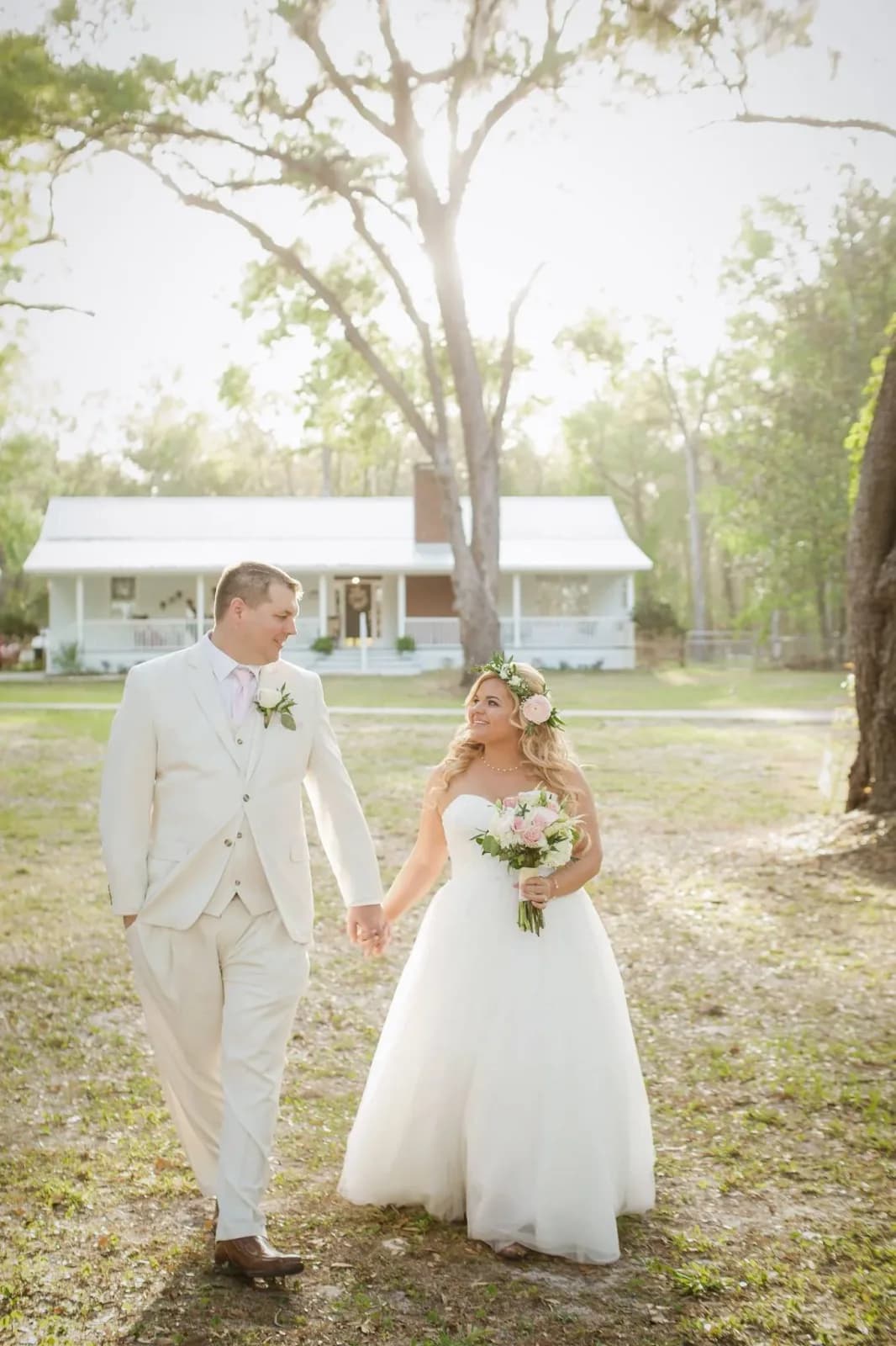 A bride and groom facing each other under a palm, the bride holding a white bouquet