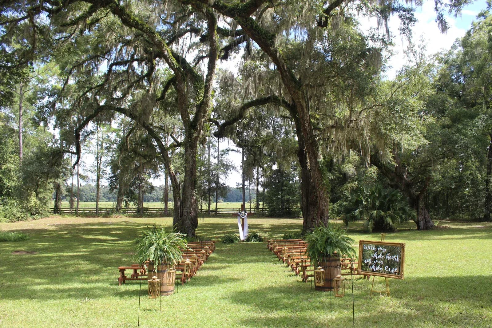 The ceremony lawn seen wide, oaks arching overhead and benches lined up on the grass