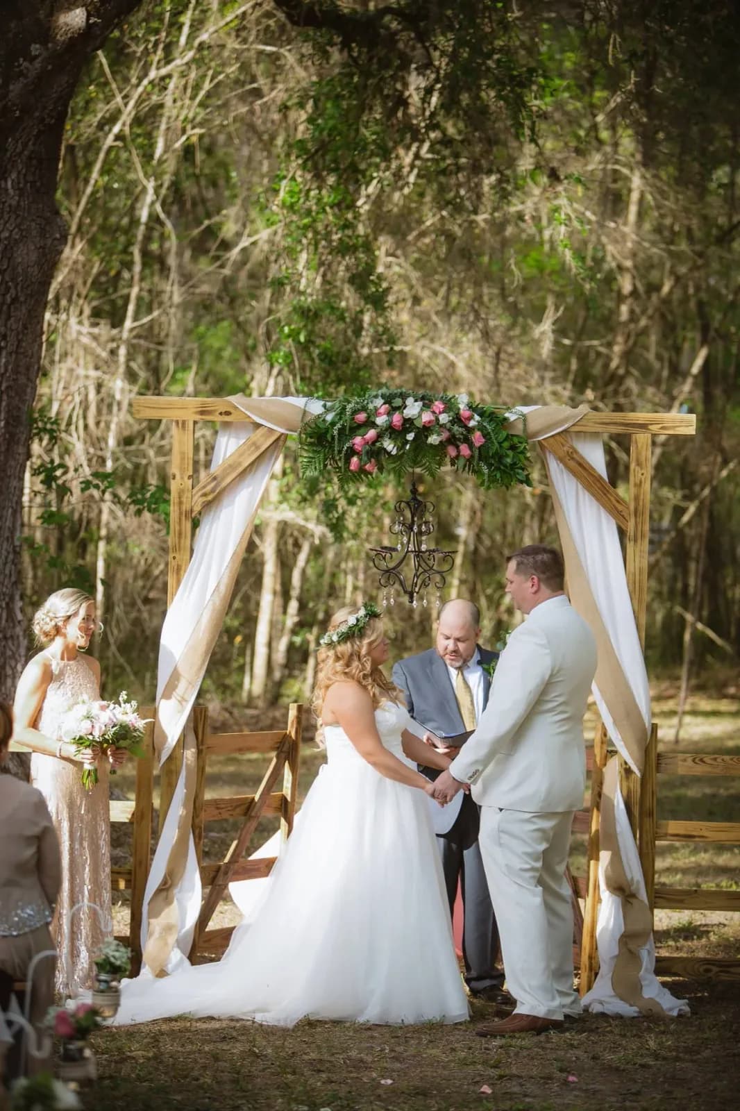A couple exchanging vows in front of the officiant beneath the draped ceremony arch