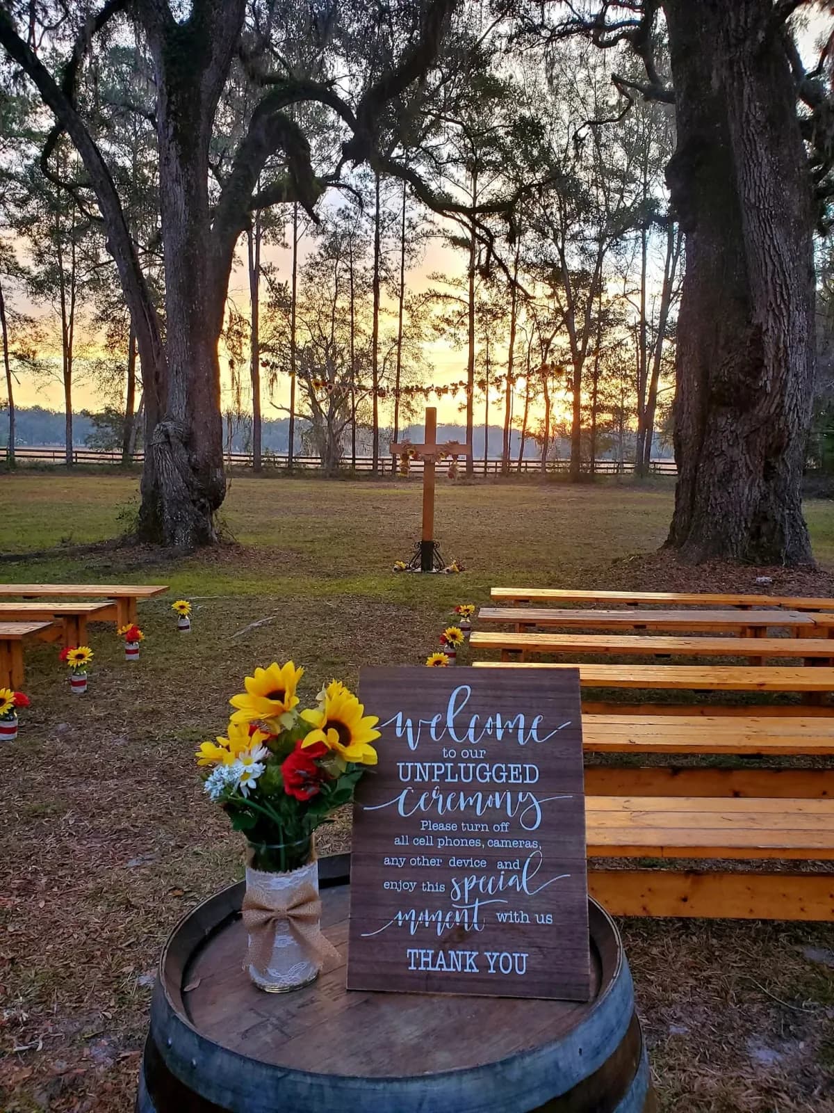 A hand-lettered welcome sign on a barrel with sunflowers, in front of the ceremony benches