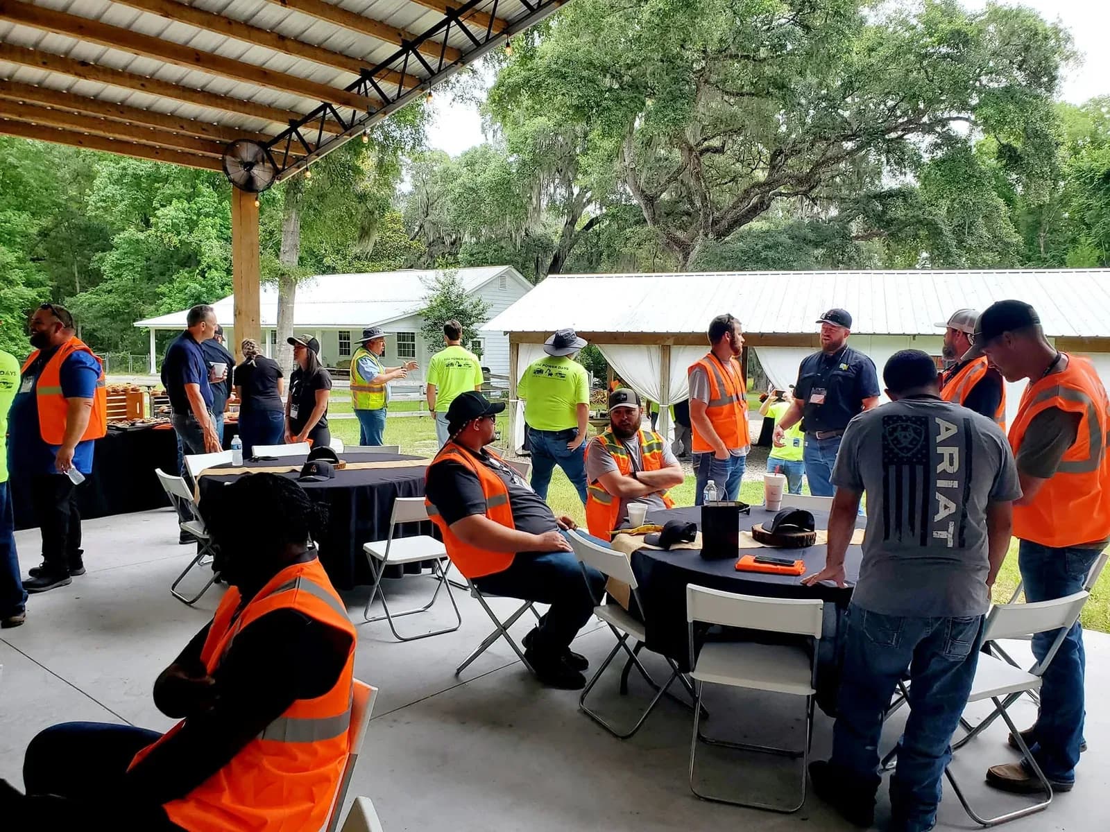 A company crew in high-visibility vests seated at tables under the pavilion for a work event