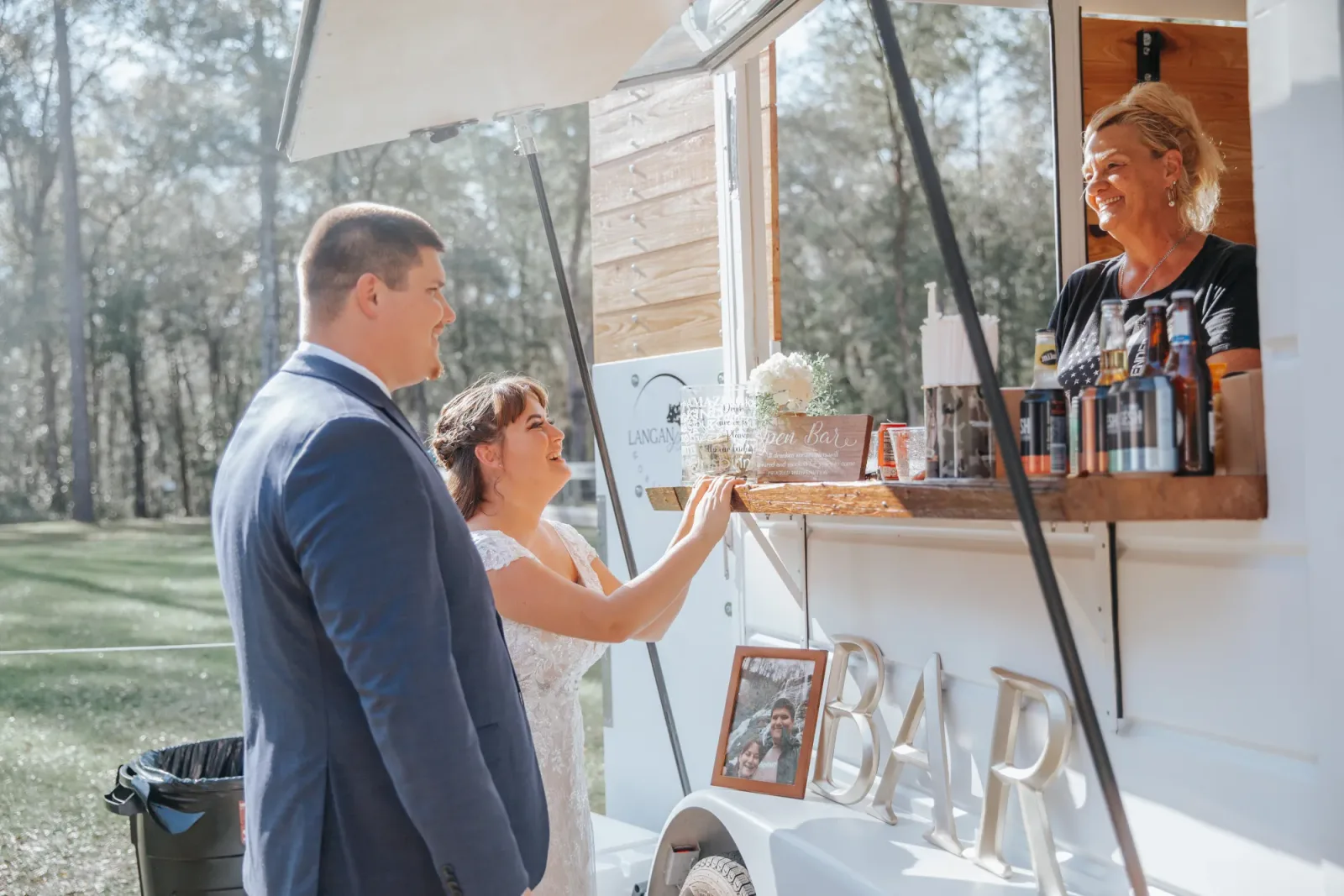 A bride and groom being served at the window of the mobile bar, the bartender handing a drink across the counter.