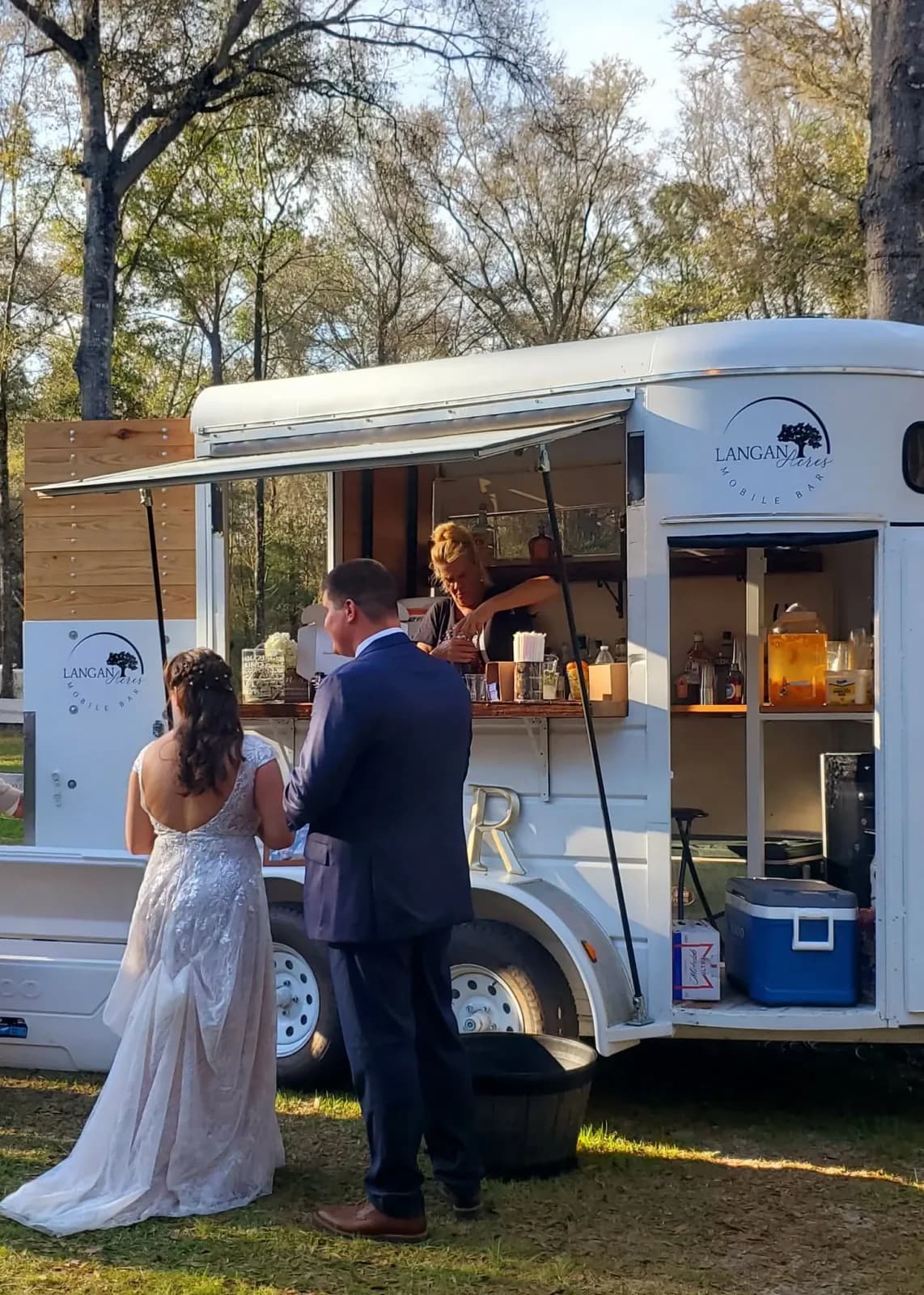 A bride in her gown being handed a drink at the window of the mobile bar