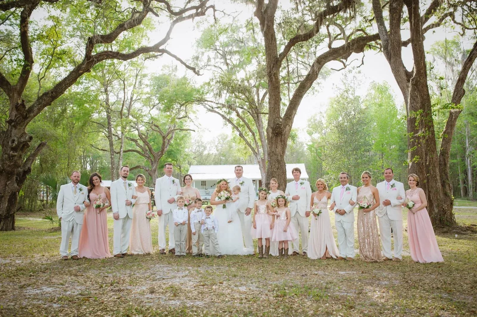 The full wedding party lined up across the lawn under the oaks, bridesmaids in blush