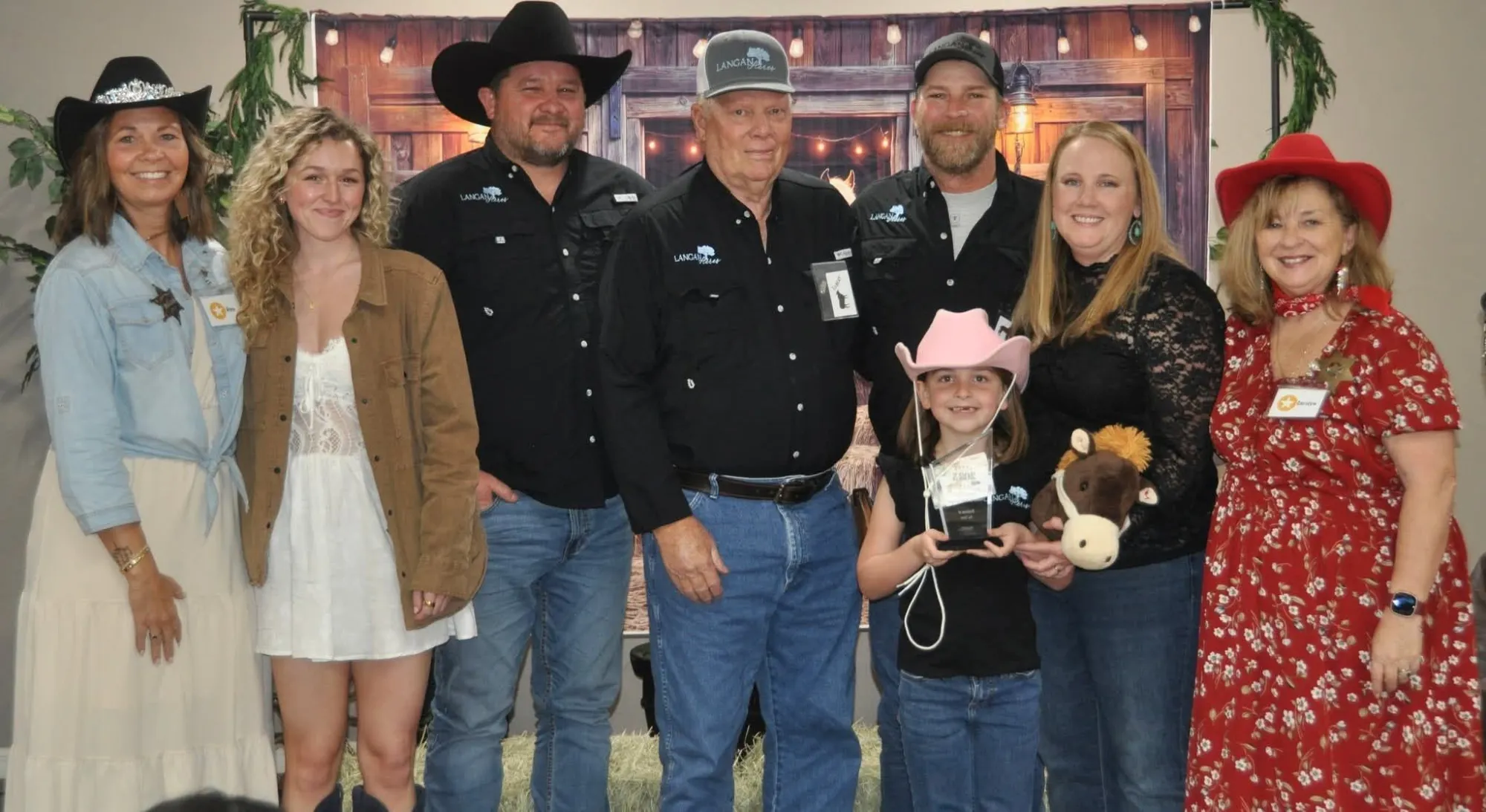 The Langan family and friends lined up on stage after the awards, their daughter in a pink cowgirl hat at the front holding the trophy.