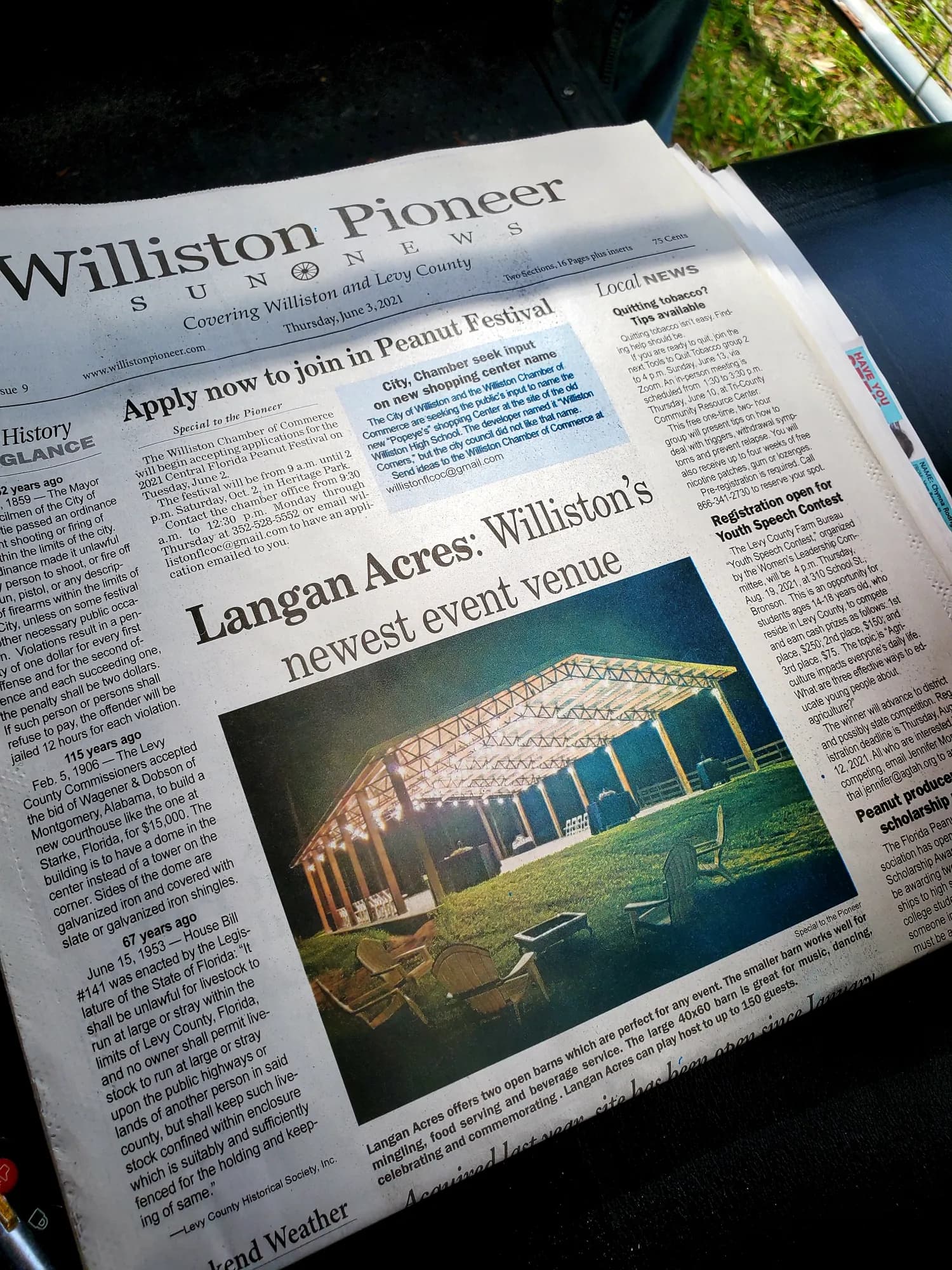 A copy of the Williston Pioneer Sun News held open, the page carrying a photograph of the pavilion under the headline “Langan Acres: Williston’s newest event venue”.